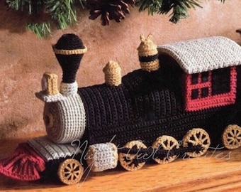 May include: A crocheted toy train with black, gray, red, and gold details. The train has a chimney, a bell, and a small bee on top. The train has six wheels and a red caboose.