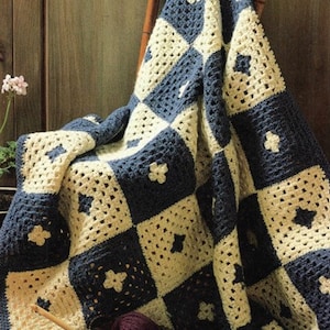 May include: A crocheted blanket with a checkered pattern in blue and cream. The blanket is draped over a wooden chair with yarn balls and a crochet hook in a basket.