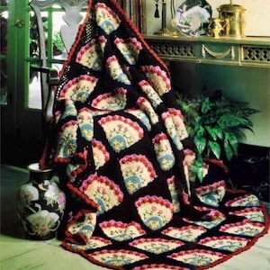 Puede incluir: Una manta de ganchillo con fondo negro y diseños florales coloridos. La manta está drapeada sobre una silla y tiene un borde rojo.