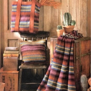 May include: A striped crocheted tote bag, pillow, and throw blanket in shades of brown, purple, orange, and green. The items are displayed on a wooden chair and table with a cactus and books.