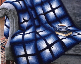 May include: A blue and white crocheted throw blanket with a gradient pattern, draped over a gray couch. A cup of tea and a book are on the couch.