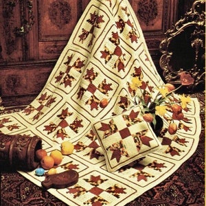 May include: A crocheted throw blanket and pillow with a patchwork design in shades of cream, brown, and red. The blanket is laid out on a brown rug with a floral pattern.