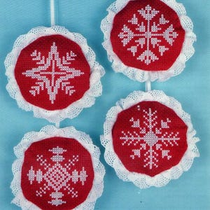 Könnte beinhalten: Vier rote und weiße gehäkelte Ornamente mit Schneeflockenmustern. Jedes Ornament ist an einer weißen Schnur befestigt.