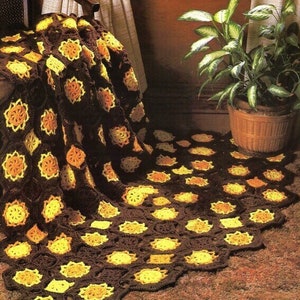 May include: A handmade crochet blanket in shades of brown, yellow, and orange. The blanket features a repeating floral pattern, with each flower framed by dark brown hexagons. The blanket is draped over a chair and spread across the floor.