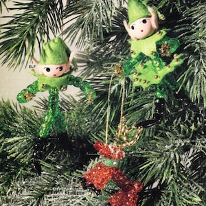 May include: Christmas tree decorations: two green felt elf figures and a red beaded reindeer. The elves have painted faces, green hats, and beaded arms and legs. The reindeer has gold antlers and a green collar.