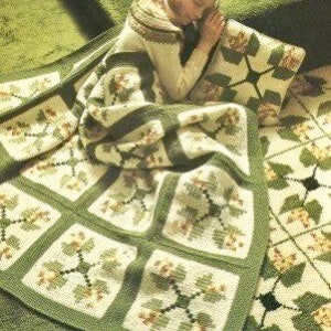 May include: A green and white crochet blanket with a floral pattern. The blanket is made up of squares with a star in the center. The blanket is on a green carpet.