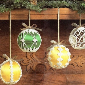May include: A collection of Christmas ornaments. The ornaments are round, with a satin or crocheted exterior. Colors include green, yellow, and white. Each ornament is suspended by a gold string and topped with a small bow. The background is a wooden surface.