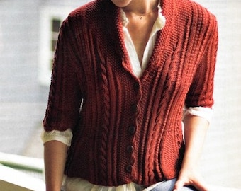 May include: A red cable knit cardigan with a V-neck and a white button-down shirt underneath. The cardigan has a relaxed fit and is worn by a person with long brown hair.