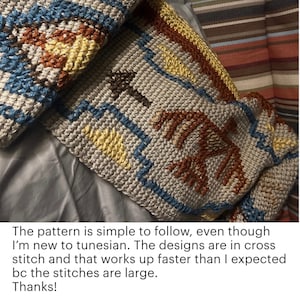 Puede incluir: Primer plano de una manta de crochet gris con un patr&oacute;n geom&eacute;trico en tonos de marr&oacute;n, amarillo y azul. La manta est&aacute; doblada por la mitad y el patr&oacute;n es visible en ambos lados.