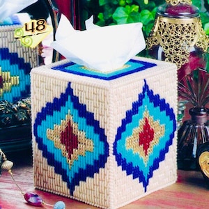 May include: A square tissue box cover with a cream-colored woven design. It features a geometric pattern in blue, turquoise, gold, and red. The top has a blue border and a square opening for tissues.