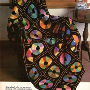 May include: A black crocheted blanket draped over a chair, featuring colorful circular designs. Each circle is divided into segments of various colors, including red, orange, yellow, green, blue, and purple. The blanket has a geometric pattern.