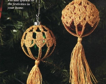 Op de afbeelding: Twee gouden gehaakte kerstballen met kwastjes die aan een groene kerstboom hangen. De ballen zijn gemaakt van gouden draad en hebben een delicaat, kantwerk-achtig ontwerp. De tekst "Trim your tree with a Midas touch Vera Sloan's TOUCH OF GOLD ORNAMENTS will add sparkle to the festivities in your home." is zichtbaar in de afbeelding.