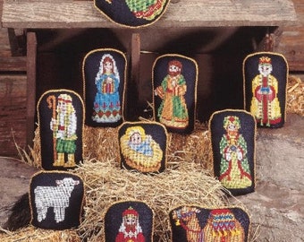 Könnte beinhalten: Ein Set mit 10 Filz-Anhängern, die die Weihnachtsgeschichte darstellen. Die Anhänger sind schwarz mit goldenen Verzierungen und zeigen gestickte Figuren von Jesuskind, Maria, Josef, den drei Weisen, einem Engel, einem Hirten, einem Schaf und einem Kamel.