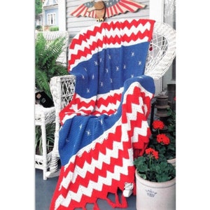 May include: A crocheted blanket in the colors of the American flag, with red, white, and blue stripes and stars. The blanket is draped over a white wicker chair on a porch.