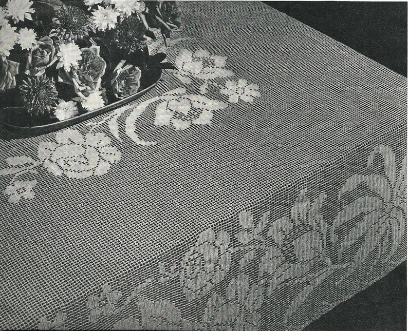 May include: A white crocheted tablecloth with a floral design. The tablecloth features a repeating pattern of roses and leaves.