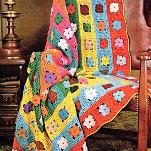 May include: A colourful crocheted blanket with a flower pattern. The blanket is made with stripes of different colours, including red, orange, yellow, green, blue, and pink. The blanket is draped over a chair.