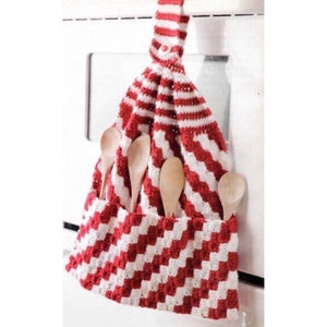 May include: A red and white striped crochet kitchen towel with a pocket holding wooden spoons. The towel is hanging from a white surface. The crochet pattern is a diagonal stripe design.