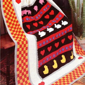 Könnte beinhalten: Eine bunte Häkeldecke mit einem karierten Rand. Die Decke zeigt verschiedene Tiermotive, darunter Schweine, Kaninchen und Enten, sowie Herzen und Blumen.