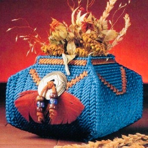 May include: A blue woven decorative container with a decorative silver-colored button, red feather, and beaded accents. The container is filled with dried flowers and wheat stalks. The container has orange and brown accents.