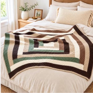 Puede incluir: Una manta de ganchillo rectangular con un patrón geométrico de rayas concéntricas en marrón oscuro, beige claro y verde salvia. El tejido presenta una textura de punto visible, dispuesta en un diseño cuadrado sobre la cama.
