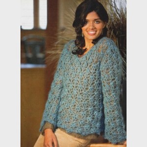 May include: A light blue, open-weave sweater with a V-neck. The long-sleeved top has a floral pattern and a loose fit. The sweater is made of a soft, possibly wool, material. The model is wearing a light brown undershirt.