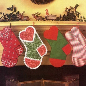 May include: Four Christmas stockings hang from a mantel. The stockings are red, green, and white, with various patterns including hearts, stripes, and floral designs. A garland and decorative figurines are above the stockings.
