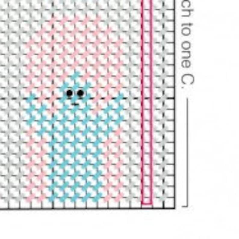 May include: A cross stitch pattern featuring a blue and pink design with a small gray ghost in the center. The pattern is on a white grid.