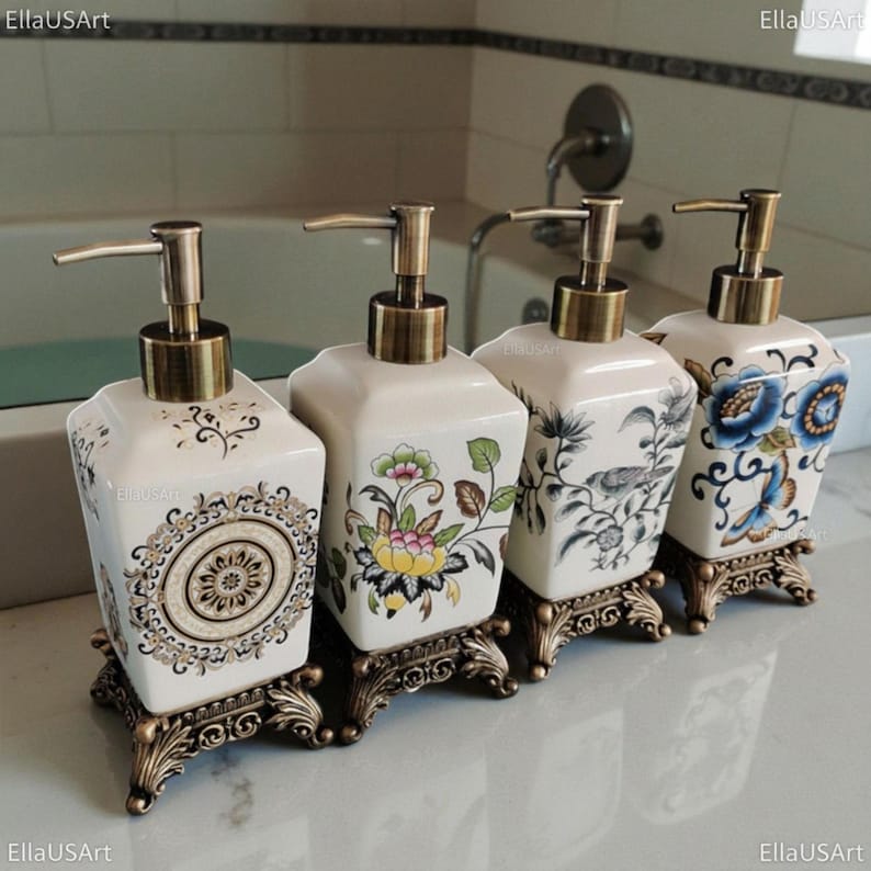 May include: Four square ceramic soap dispensers with bronze-toned pump mechanisms and ornate, decorative bronze-toned bases. Each dispenser features a unique pattern, including a central mandala, a floral motif, a bird illustration, and blue flowers.