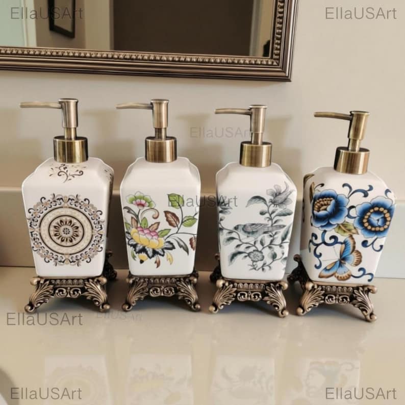 May include: Four square ceramic soap dispensers with antique bronze-toned pump mechanisms and ornate, decorative metal bases. Each dispenser features a unique pattern: a central mandala, colorful floral vines, a bird on a branch, and blue flowers with a butterfly.