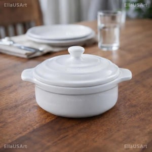 May include: A white ceramic casserole dish with a matching lid and two side handles. The round pot features a smooth, glossy finish and a stepped lid design. The piece is centred, showcasing its clean, minimalist form and functional construction.