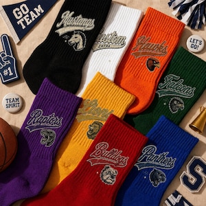 May include: A collection of eight crew socks in various colors including black, white, orange, green, purple, yellow, red, and blue. Each sock features a team name in a vintage-style font and a corresponding animal mascot graphic.