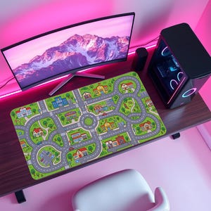 May include: A rectangular desk mat featuring a colorful illustrated city map with winding gray roads, green grass, trees, and various buildings including a school, police station, and houses, all printed on a flat surface with rounded corners.