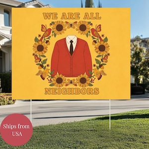 May include: A yellow yard sign with the text "WE ARE ALL NEIGHBORS" in brown lettering. The sign features a red cardigan, surrounded by sunflowers, birds, and butterflies. The sign is displayed on a green lawn.