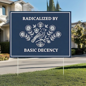 Pode incluir: Um letreiro de jardim azul marinho com texto branco e um desenho floral e de pássaro branco. O texto diz "RADICALIZED BY BASIC DECENCY". O letreiro é exibido em um gramado verde com uma casa ao fundo.