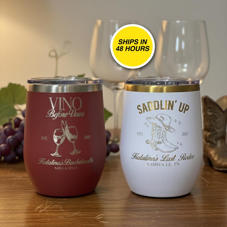 May include: Two insulated wine tumblers. One is burgundy with "VINO Before Vous" text and a wine glass graphic. The other is white with "SADDLIN' UP" text and a cowboy boot graphic. Both have metallic silver lids.