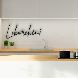 Könnte beinhalten: Eine moderne Küche mit weißer Arbeitsplatte und Schränken. Ein Edelstahlbecken, ein Kochfeld mit zwei Töpfen und der Text "Likörchen?" in schwarzer Schrift sind zu sehen.