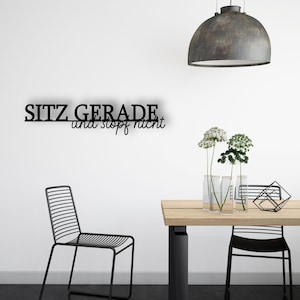 Könnte beinhalten: Eine moderne Innenszene mit einem schwarzen Metallstuhl, einem Holztisch und einem Metallschild an der Wand mit der Aufschrift "SITZ GERADE und stopf nicht". Die Szene wird von einer Hängelampe beleuchtet und umfasst Blumenarrangements.