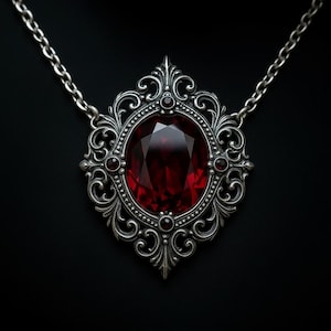 Puede incluir: Collar con colgante plateado con una gema roja oscura ovalada y facetada. El colgante tiene un diseño de filigrana ornamentado con pequeños detalles rojos. La cadena es de eslabones plateados delicados. El fondo es negro.