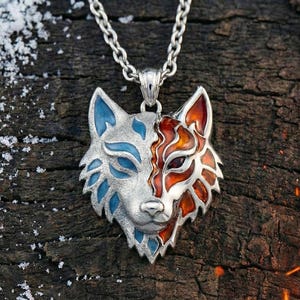 May include: A silver wolf pendant with a split design, half blue and half orange, on a silver chain. The pendant is set against a dark wood background with snow.
