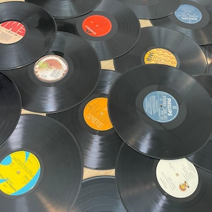 Könnte beinhalten: Eine Sammlung schwarzer Schallplatten mit farbenfrohen Etiketten. Die Etiketten zeigen verschiedene Farben, darunter Orange, Rot, Blau und Gelb. Die Schallplatten sind verstreut und zeigen eine Vielzahl von Albumcovern und Logos von Plattenfirmen.