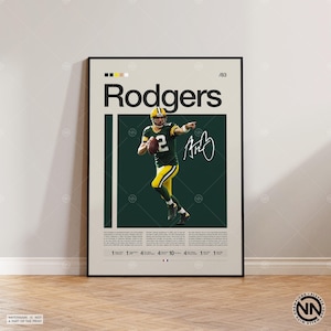 May include: A framed poster featuring a football player in a green and yellow uniform, throwing a football. The poster has the name "Rodgers" in large text, a signature, and the number "2". The background is dark green.