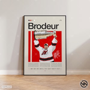 May include: Poster featuring Martin Brodeur holding the Stanley Cup, wearing a New Jersey Devils jersey. The poster has a red and cream color scheme with the name "Brodeur" in large text. Includes a signature and the number 31.