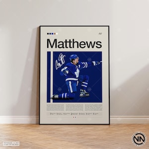Puede incluir: Póster enmarcado en negro con un jugador de hockey con uniforme azul, arrodillado sobre un fondo azul. El nombre del jugador, "Matthews", se muestra en letras grandes, junto con su firma y el número "97".