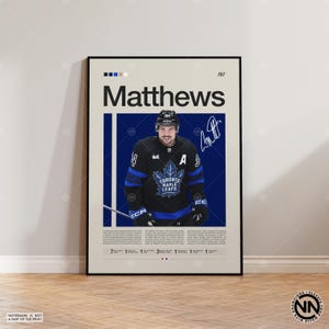 Puede incluir: Póster con un jugador de hockey con una camiseta negra y azul de los Maple Leafs de Toronto. El póster incluye el nombre del jugador, Matthews, y una firma. El fondo es de color beige claro con una franja vertical azul.