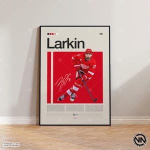May include: A framed poster featuring a hockey player in a red uniform, with the name "Larkin" in large letters. The poster has a red and beige color scheme, with the player's signature and the number 71 visible.