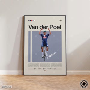 Puede incluir: Póster enmarcado del ciclista Van der Poel con uniforme ciclista azul y blanco, celebrando una victoria. El póster tiene un fondo beige con el nombre y la firma del ciclista. El póster está enmarcado en negro y expuesto sobre un suelo de madera.