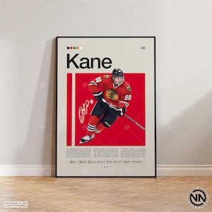 May include: A framed poster featuring a hockey player in a red and black uniform with the number 88. The poster has the name "Kane" in large letters, a signature, and a red background. The poster is displayed on a light-colored wall.
