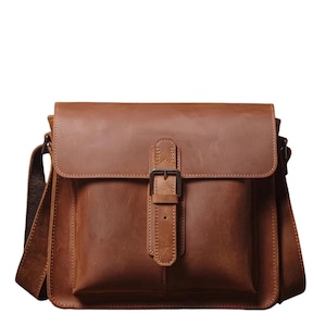 May include: A brown leather messenger bag with a flap closure and adjustable shoulder strap. The bag features a front pocket with a buckle closure and a textured finish. The bag is designed for carrying items and has a classic, vintage style.