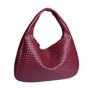 May include: A burgundy hobo bag with a woven texture. The bag has a single, curved handle and a rounded shape. The material appears to be leather or a leather-like material.