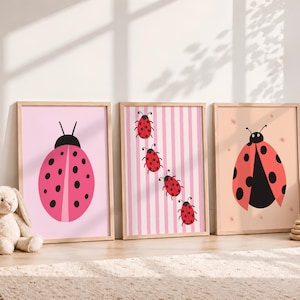 Puede incluir: Tres cuadros de pared con ilustraciones de mariquitas. El primero muestra una mariquita rosa grande sobre un fondo rosa claro. El segundo presenta cuatro mariquitas pequeñas sobre un fondo de rayas rosas. El tercero muestra una mariquita roja.